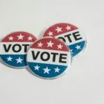 Przypinki wyborcze w barwach czerwonej, białej i niebieskiej na białym tle