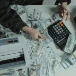 Ręce liczące banknoty 100 dolarów obok kalkulatora na biurku