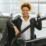 Uśmiechnięta kobieta z kluczykami przy samochodzie w salonie dealerskim