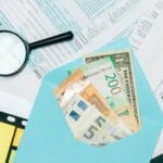 Dokumenty podatkowe i banknoty w niebieskiej kopercie z lupą