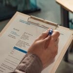 Terminy płatności na fakturach: jak je ustawiać, by poprawić cash flow Dłoń trzymająca firmową fakturę na clipboardzie obok trzymanego długopisu