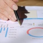 Dłoń z długopisem wskazująca wykresy finansowe na dokumencie