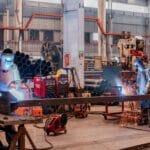 Polityka przemysłowa państwa: jakie branże dostają wsparcie i jakie warunki trzeba spełnić? Spawacze w kaskach ochronnych pracujący w hali przemysłowej