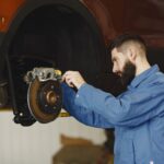 Mechanik w niebieskim kombinezonie wymienia hamulce w aucie w warsztacie