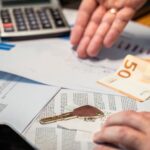 Dłonie przeglądające dokumenty finansowe, banknot 50 euro i klucz